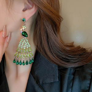 Close-up of long peacock tassel earrings with green crystals on a model wearing them