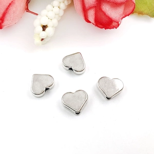 Macro view of four silver heart-shaped metal spacer beads for DIY jewelry on white background