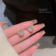 Detail of heart stud earring with pearls and blue zircon held by a model hand