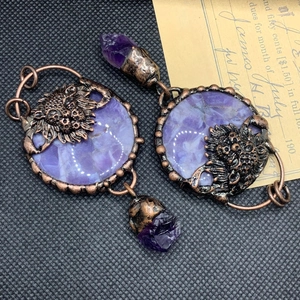 Detail of vintage bronze earrings with lion relief, purple gemstones and raw crystals