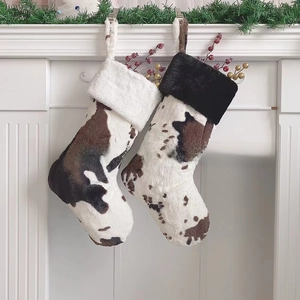 Pair of cow print Christmas stockings with plush cuffs hanging on a fireplace