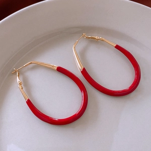 Détail des boucles d'oreilles ovales en émail rouge et or sur une assiette en porcelaine blanche