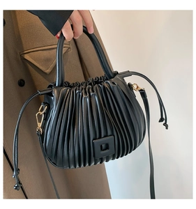 Detail of black pleated bucket bag with square buckle and adjustable side drawstrings