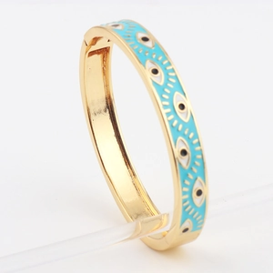 Detail view of gold-plated bangle with blue evil eye enamel patterns on white background