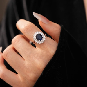 Detail of elegant silver ring with deep blue zircon and double halo on model's hand