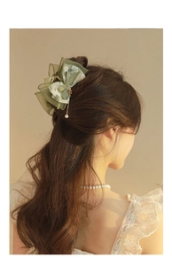 Detail of green tulle bow hair clip with floral print and elegant pearl pendant tassel