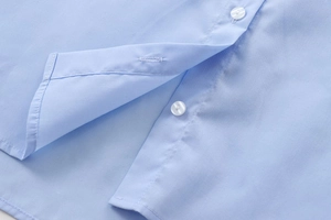 Macro shot of light blue cotton shirt featuring neat buttons and precise stitching details