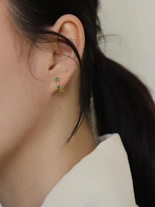 Gros plan d'une créole en argent 925 doré avec trois zircons verts portée par un mannequin