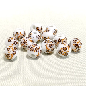 Macro detail of 10mm white ceramic beads with brown flower and orange leaf patterns
