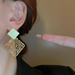 Detail view of gold woven mesh geometric stud earrings worn on ear for sizing