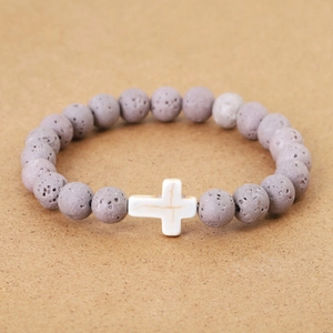 Detailed shot of volcanic stone beads with a white cross pendant on a textured surface
