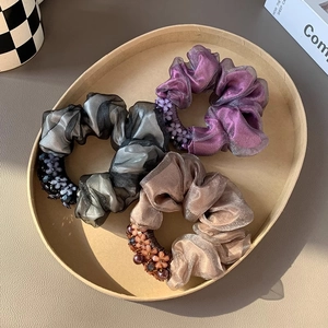 Three-piece mesh scrunchie set in purple, gray, and beige with floral bead accents on a tray
