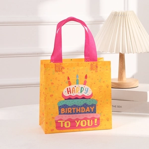 Detail of yellow non-woven birthday gift bag with colorful cake print and pink handles