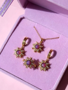 Detail of gold sunburst jewelry set with purple opal and cubic zirconia in a velvet box