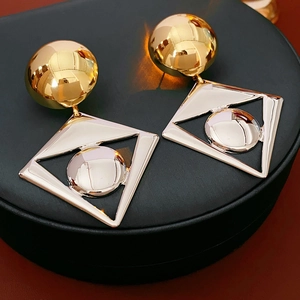 Macro detail of geometric two-tone metal earrings with gold sphere and silver triangle