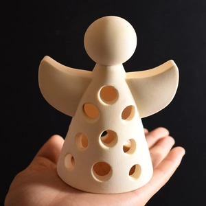 Close-up of a hand holding an ivory angel figurine with hollow cutouts for DIY home decor