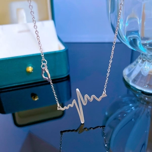 Polished silver heartbeat pendant necklace with small heart charm on reflective surface