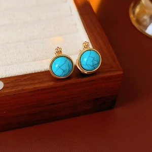 Détail macro de boucles d'oreilles vintage dorées avec résine turquoise sur un plateau à bijoux