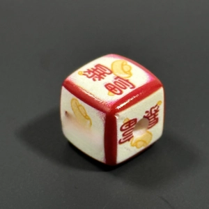Macro shot of white acrylic square bead with red trim and golden ingot fortune motif