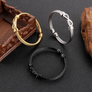 Three-color infinity cable wire bracelets in gold, silver, and black on dark stone