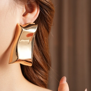 Gros plan d'une grande boucle d'oreille dorée géométrique portée par une femme