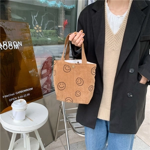 Detailed view of a brown corduroy tote bag with black smiley face prints and a metal snap button
