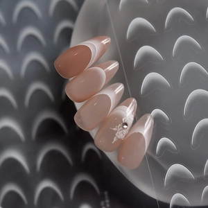 Macro view of almond nude pink french nails with white rose detail and small diamond