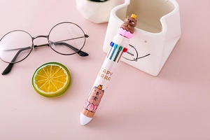 Close-up of a 10-color Capybara ballpoint pen on a pink desktop with lifestyle props