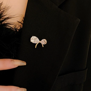 Detailed close-up of a gold bow brooch with sparkling zircons pinned to a black blazer