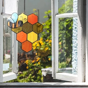Detail of bee and honeycomb suncatcher hanging on a vintage wooden window in a garden