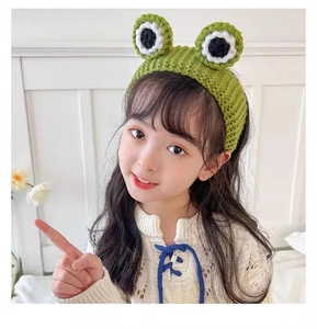 Detail of child wearing a green knitted frog eye headband in a bright bedroom setting