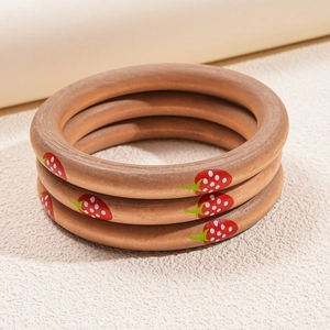 Detailed view of three stacked wooden bangles with hand-painted strawberry motifs