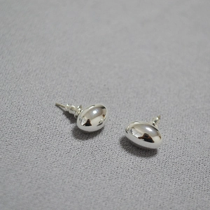 Macro shot of silver bean stud earrings with polished metallic mirror finish surfaces