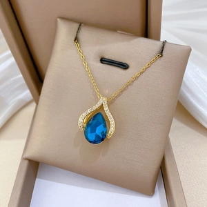 Close-up of a blue water drop pendant with sparkling crystals on a golden necklace chain