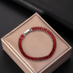 Silver tennis bracelet featuring rectangular red zircon stones on a champagne gift box