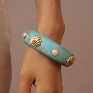 Détail du bracelet en résine bleu marbré avec décor de coquillage doré et perles