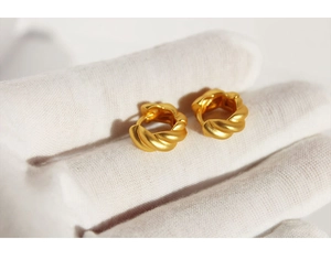 Close-up of matte gold twisted hoop earrings held in a white gloved hand showing texture