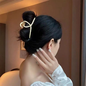 Detail of a golden metal hair claw clip with cross-curve design on an elegant updo hair