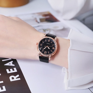 Detailed view of women's quartz watch with gold case and black leather strap on wrist
