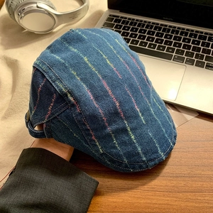 Detail of blue denim beret with colorful stitching and adjustable strap on a desk