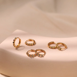 Elegant gold huggie earrings set with colorful zircon gemstones on a wavy stand