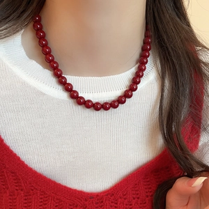 Close-up of a deep red glass beaded necklace worn by a model with a knit sweater