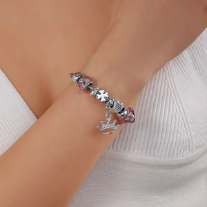 Detail of silver crown charm bracelet with pink beads worn on a model's wrist