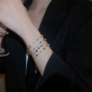 Close-up of four layered gold bracelets with colorful zircons and adjustable sliding clasps