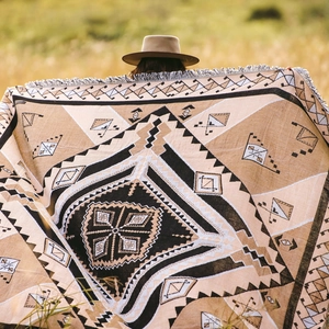 Bohemian geometric woven camping blanket with tassels shown in a scenic outdoor setting