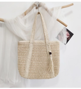 Detail of woven straw tote bag with wood bead tassel hanging on wooden display