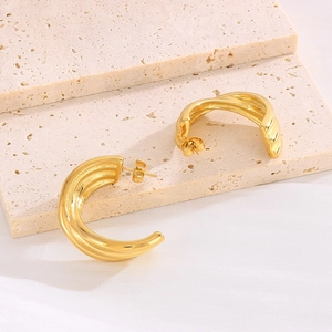 Macro shot of gold C-shaped twisted texture earrings on decorative beige stone blocks