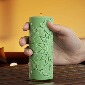 Detail of hand-held green cylindrical candle with 3D sun and moon mandala carvings