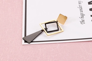 Macro detail of geometric black and gold irregular shape long earrings on pink background