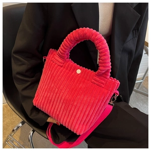 Detail of rose red corduroy bucket bag with textured handle held against black suit